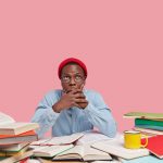 surprised-dark-skinned-man-covers-mouth-with-both-hands-tries-be-speechless-focused-upwards-wears-red-hat-and-shirt-poses-at-desktop