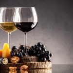 front-view-wine-glasses-fresh-grapes-walnuts-yellow-cheese-on-wood-board-overturned-bottle-on-dark-background