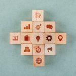 Business strategy concept with wooden blocks with icons on sage color background flat lay. horizontal image